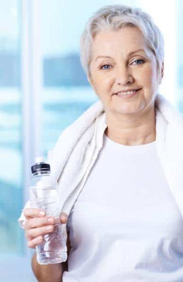 Portrait of pretty senior woman with bottle of water in gym